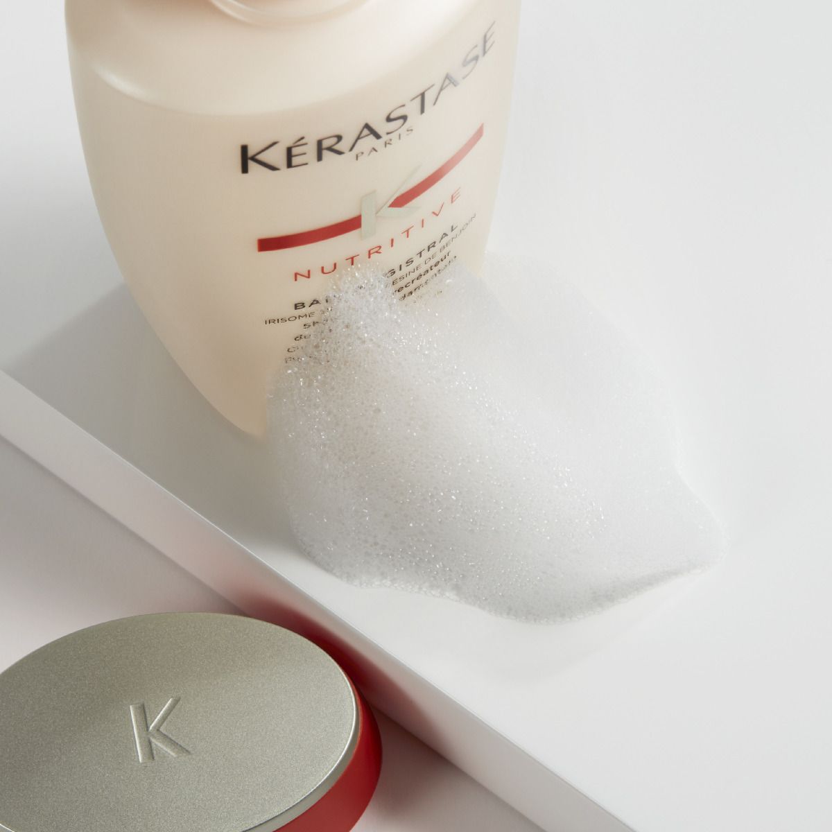 een productfoto van de kerastase nutritive shampoo met een beetje schuim erbij